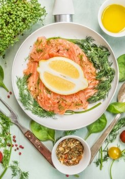 Raw salmon in white pan with lemon, spices, fresh herbs and fork, top view, close up