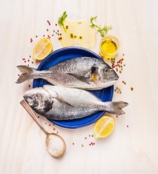 Raw dorado fish in blue plate with spilled oil ,salt,herbs and spices on white wooden background , top view