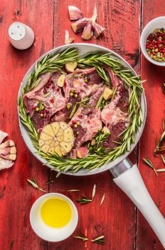 Raw double lamb loin chops meat in white pan with herbs,oil and spices on red wooden background, top view, close up
