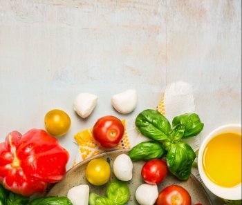 Tomatoes, mozzarella balls with basil leaves and oil in white bowl on rustic wooden background, top view, place for text