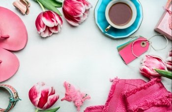 Springtime womens workspace with tulips flowers, pink clothes and shoes, tags and coffee cup, top view, frame