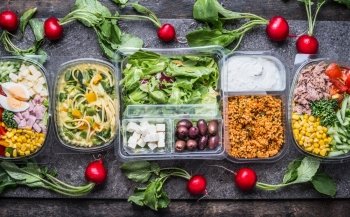 Variety of clean dieting salads in  plastic package and green measuring tape on rustic background, top view. Healthy clean food concept.