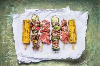 Various Meat Skewers  for grill with vegetables , corn ears and condiment on green rustic background , top view