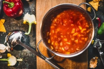 Hot Mexican spicy soup in cooking pot with ladle on rustic kitchen table background, top view.