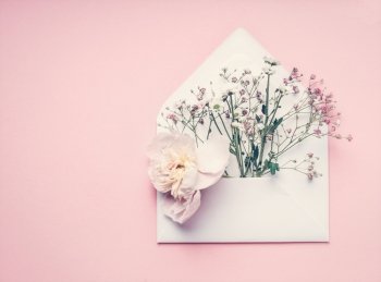 Opened envelop with flowers arrangement on pastel pink background, top view, copy space. Creative greeting, Invitation and holiday concept
