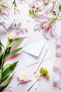 Blank white envelop with pencil and various decoration equipment and flowers on pink pale table background, top view. Festive Invitation , Creative  greeting and holiday, concept
