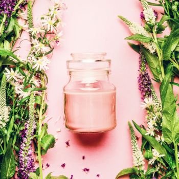 Natural herbal skin care cosmetic concept. Glass jar with cream and fresh herbs and flowers on pink background, top view, copy space, square.  Beauty, skin and hair care concept