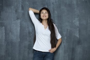 Asian young woman looking up standing by wall 