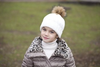 Portrait of beautiful little girl in a white knitted hat autumn
