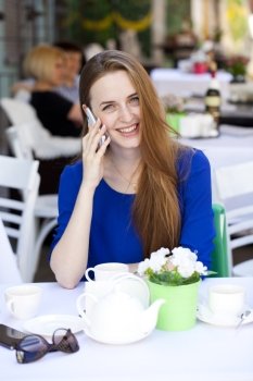 Happy Beautiful young blonde woman calling by phone sitting in a coffee shop 
