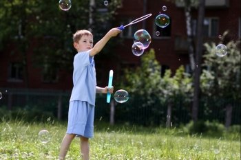 little boy is played with soap bubbles in the street