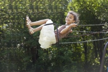 Happy little girl riding on a swing in the park