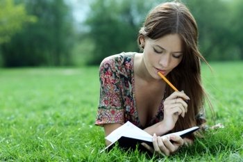 Young beautiful woman lays on a grass in park with a diary in hands 
