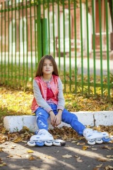 Portrait of a ten-year girl sits on a playground in roller skates