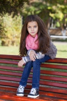 Beautiful little girl sitting on a bench in autumn park