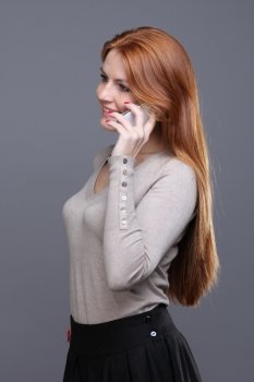 Closeup portrait of a cute young woman talking on mobile phone against grey background 