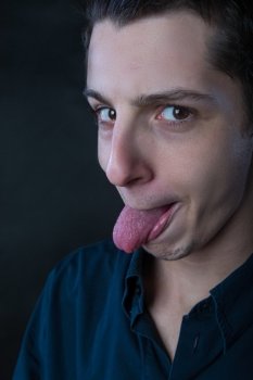 portrait of young man wearing blue shirt making silly faces against black background