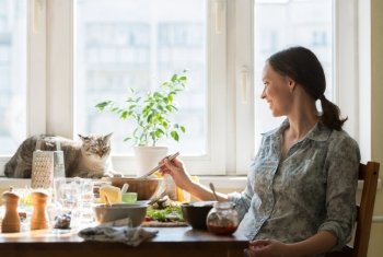 Woman cooking pizza at home. Filling dough with ingredients, while cat relaxing on window