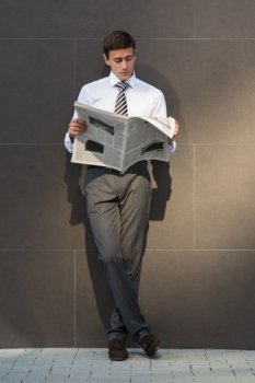 Handsome businessman or manager, in front of modern office architecture, reading newspaper