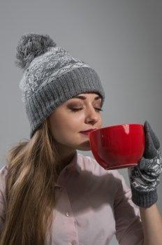 Woman in winter clothes enjoying a hot drink eyes closed on gray background