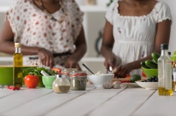 Two unrecognizable african women cooking in kitchen making healthy food salad with vegetables