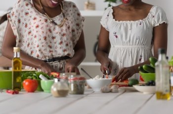 Two unrecognizable african women cooking in kitchen making healthy food salad with vegetables