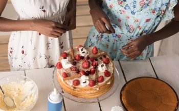 Unrecognizable african women at the kitchen cooking cake with strawberry