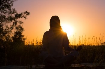 Silhouette of a beautiful Yoga woman on sunrise and rays of light surrounding her