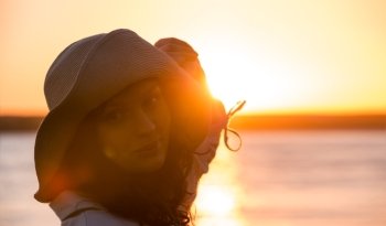 Woman wearing straw hat smiling and having fun against sunset and beautiful sea
