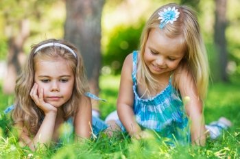 Two little sisters having fun in summer park while laying on lawn