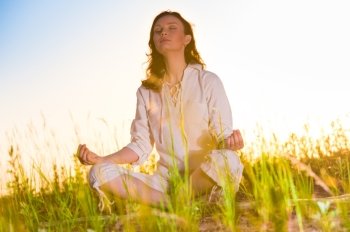 Yoga woman meditating on green grass against the sun