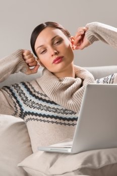Portrait of a young woman sitting in front of her laptop on sofa and stretching her arms