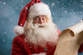 Portrait of happy Santa Claus reading Christmas letter outdoors at north pole at snowfall