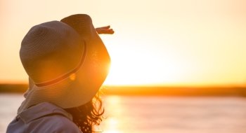 Young and beautiful woman wearing a hat in sunset light looking far away. Photo from behind