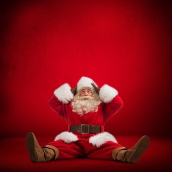 Hilarious and funny Santa Claus sitting on floor and looks frustrated on a red background full length