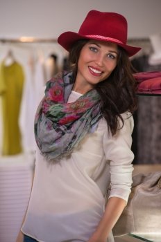 Beautiful woman shopping in clothing store standing near shelf and wearing red hat
