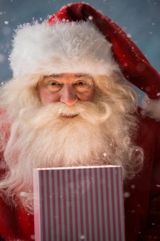 Portrait of happy Santa Claus opening gift box outdoors at North Pole. Magical light from box on his face