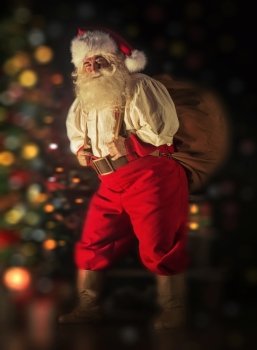 Portrait of Santa Claus carrying huge sack with presents indoor at home near Christmas tree