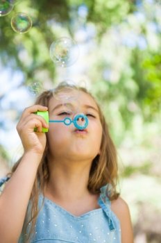 Little girl blowing soap bubbles outdoors at park