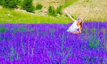 Cute female in white hat and dress enjoying beautiful purple lavender flowers field, summer time nature, travel and vacation concept