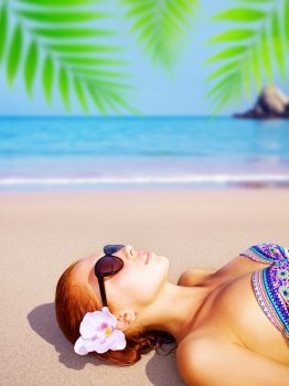 Picture of young beautiful lady on the beach, attractive female enjoying dayspa on seashore in luxury spa resort, sexy girl with orchid flower in red hair lying down on ocean coastline
