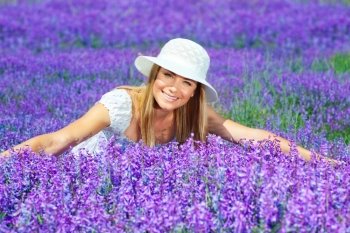Pretty woman lying down on lavender field, beautiful happy female sitting on purple flowers meadow, cheerful smiling girl enjoying violet floral glade, portrait of young cute lady over lilac plant