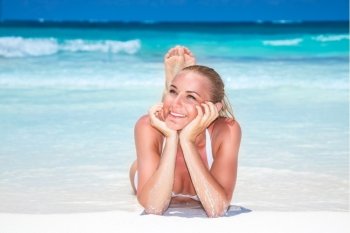 Beautiful woman on the beach, lying down and tanning on a white sandy seashore, enjoying summer vacation on a tropical beach resort