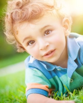 Closeup portrait of a cute little baby boy lying down on the grass, having fun in the park, spending summer holidays outdoors