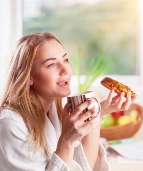 Beautiful woman enjoying tasty morning meal, drinking tea with sweet delicious bun, having breakfast in the hotel
