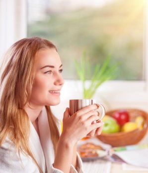 Portrait of cute blond girl drinking morning coffee on the kitchen at home, enjoying breakfast, happy domestic lifestyle