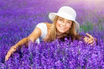 
Beautiful woman in sunny day wearing sun hat and sitting in fresh purple flower field, enjoying beauty of nature