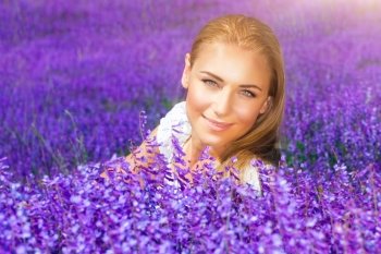 Portrait of beautiful blond woman sitting on fresh lavender field, enjoying gentle purple flowers, with pleasure spending sunny day in countryside