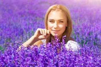 Portrait of beautiful blond woman sitting on fresh lavender field, enjoying gentle purple flowers, with pleasure spending sunny day in countryside