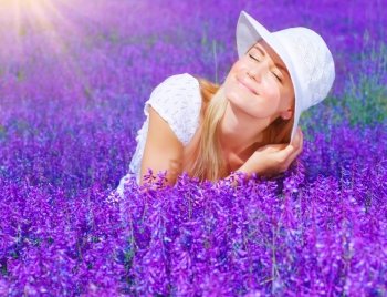 Pretty woman sitting on lavender field at sunny day, beautiful female on purple flowers meadow, cheerful smiling girl enjoying violet floral glade and sun light, portrait of young lady